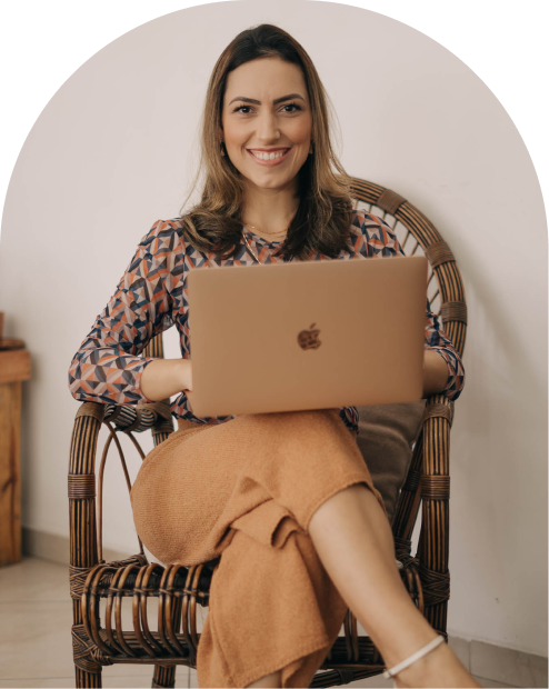 Retrato da arquiteta Nayara Barros, sentada numa poltrona de vime com um notebook no colo